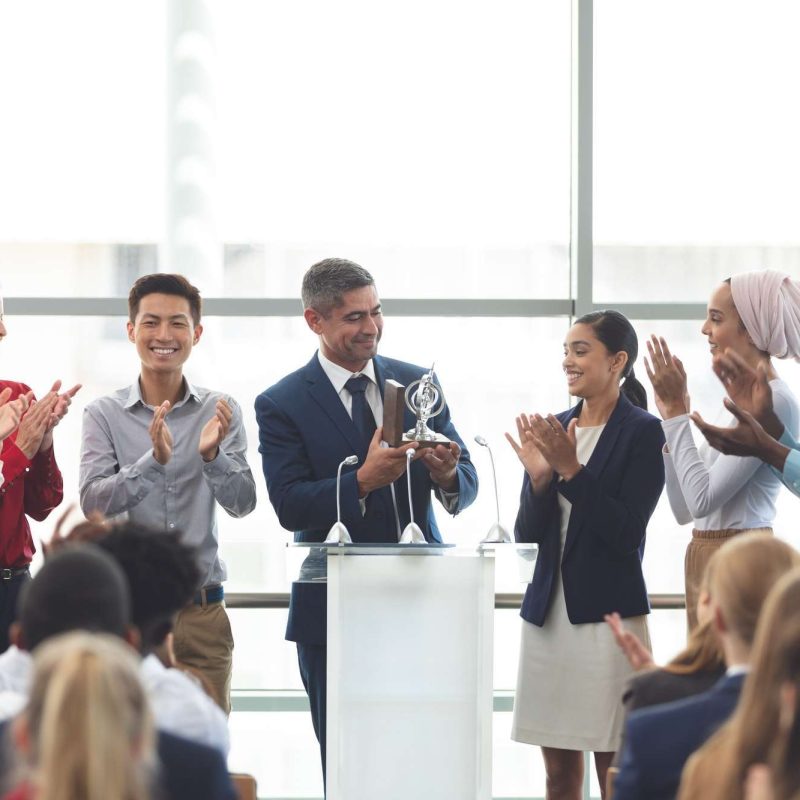 businessman-holding-award-on-podium-with-colleagues-at-business-seminar.jpg